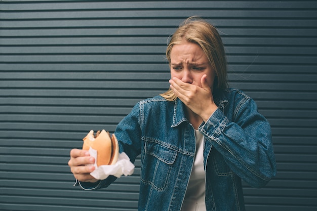 Joven mujer comiendo comida rápida al aire libre y se siente muy mal