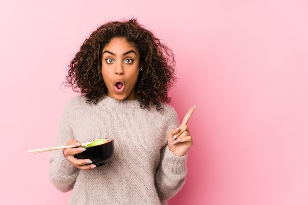 Joven mujer comiendo fideos apuntando hacia el lado