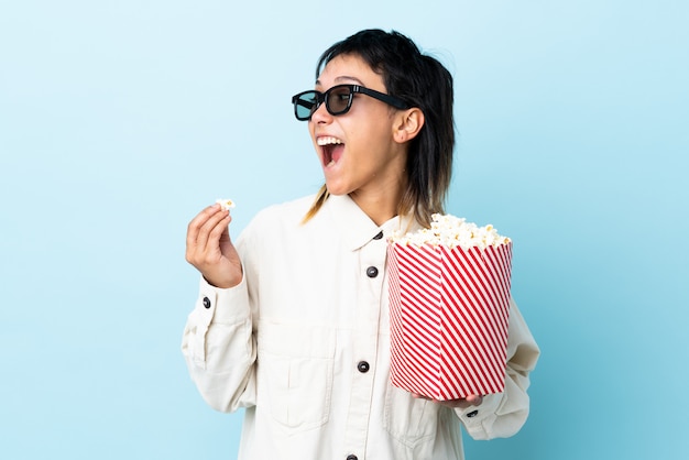 Joven mujer comiendo palomitas de maíz sobre pared aislada