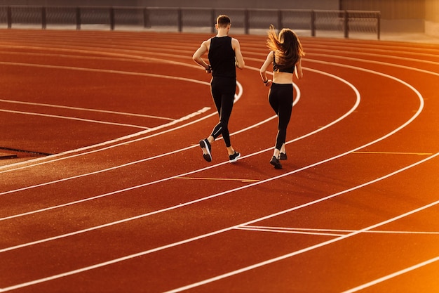 Joven y mujer corriendo en la pista de carreras en el estadio Jóvenes atletas masculinos y femeninos practicando toge