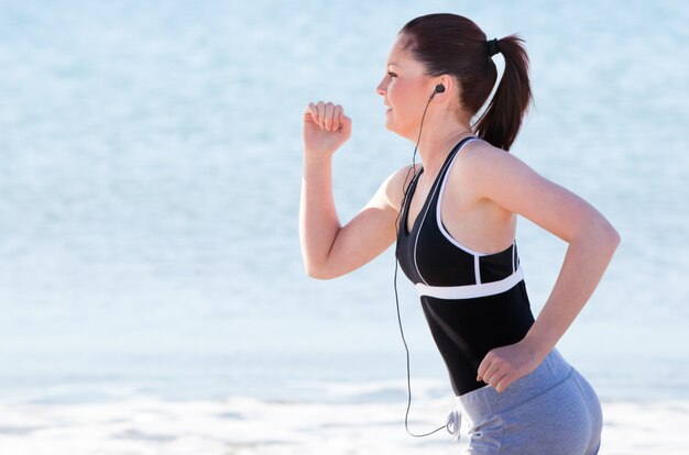 Joven mujer corriendo en la playa escuchando música