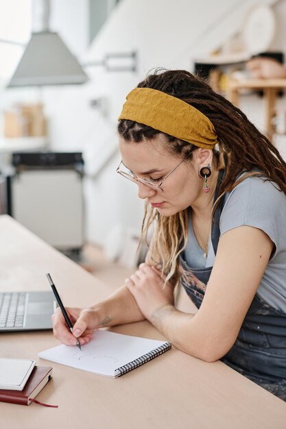 Foto joven mujer creativa haciendo notas o bocetos de un nuevo producto en el bloc de notas