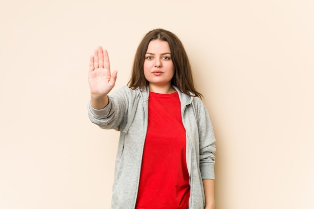 Joven mujer con curvas deportiva de pie con la mano extendida que muestra la señal de stop, impidiéndole.