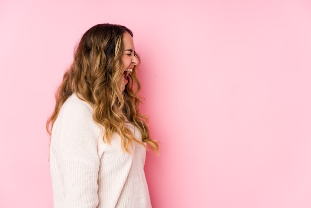 Joven mujer con curvas posando en una pared rosa aislada gritando hacia un espacio de copia