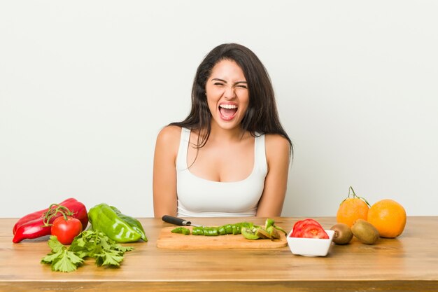 Joven mujer con curvas preparando una comida saludable gritando muy enojado y agresivo