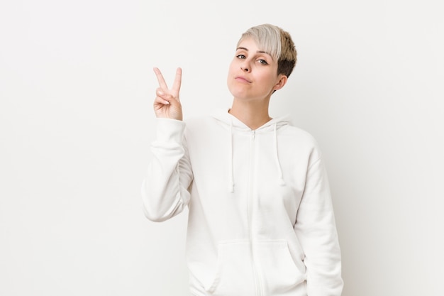 Joven mujer con curvas con una sudadera con capucha blanca que muestra el número dos con los dedos.