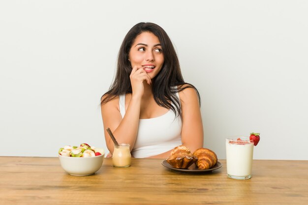 Joven mujer con curvas tomando un desayuno relajado pensando en algo mirando un espacio de copia.