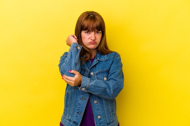 Foto joven mujer curvilínea caucásica aislada sobre fondo amarillo con dolor de cuello debido al estrés, masajeando y tocándolo con la mano.