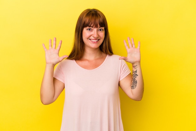 Joven mujer curvilínea caucásica aislada sobre fondo amarillo que muestra el número diez con las manos.