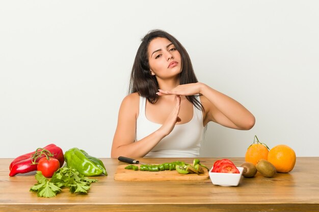 Joven mujer curvilínea preparando una comida saludable mostrando un gesto de tiempo de espera.