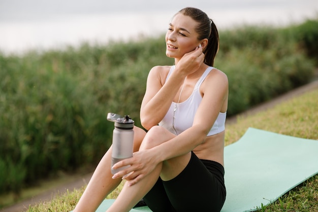 Joven mujer delgada con auriculares y teléfono inteligente escucha música en el parque en el día soleado