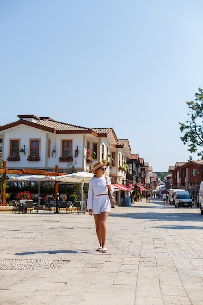 Una joven mujer delgada y bronceada con pantalones cortos blancos y una camiseta con gafas de sol y un sombrero Camine en un día caluroso y soleado en la ciudad antigua