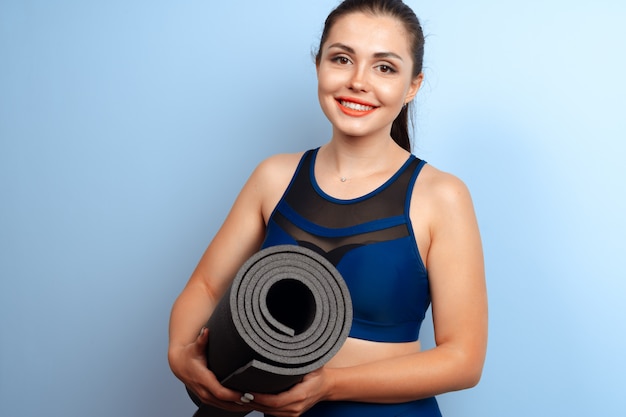 Joven mujer delgada con estera de yoga fitness en sus manos