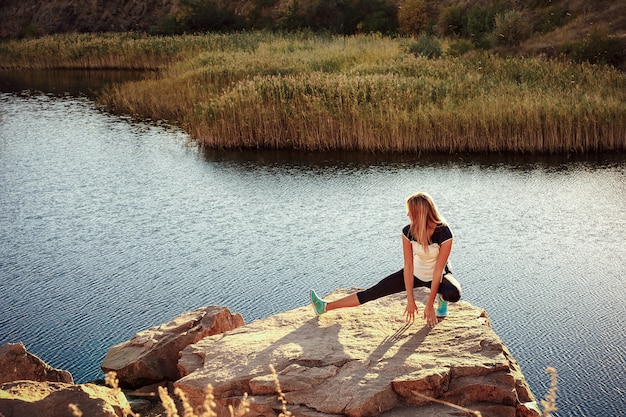 Joven mujer delgada practicando yoga al aire libre en la orilla de piedra del río de montaña. Unidad con el concepto de naturaleza