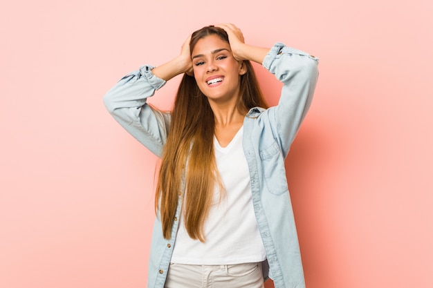 Foto joven mujer delgada ríe alegremente manteniendo las manos sobre la cabeza. concepto de felicidad