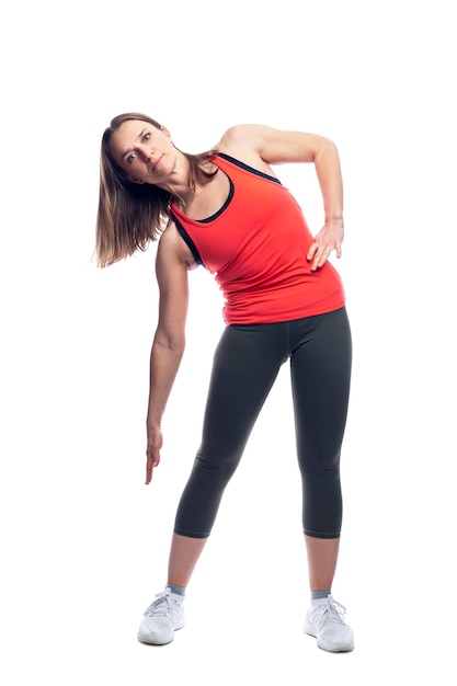 Una joven mujer delgada en ropa deportiva está haciendo gimnasia mientras está de pie Actividad y salud Aislada sobre fondo blanco Vertical Altura completa