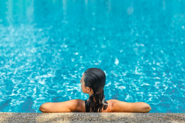 Joven mujer delgada sexy relajante en piscina tropical con agua azul cristalina en caluroso día de verano