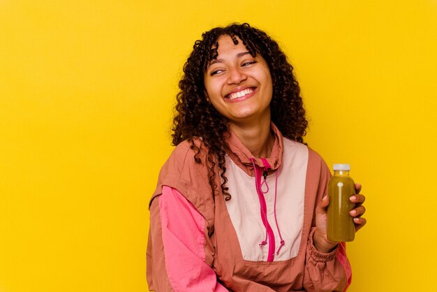 Joven mujer de deporte de raza mixta sosteniendo un batido aislado en amarillo