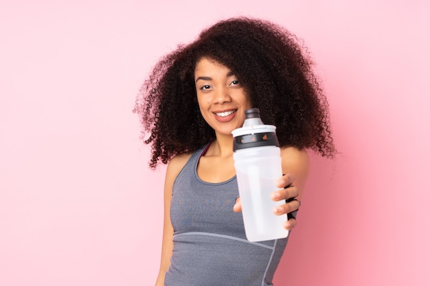 Joven mujer deportiva afroamericana aislada en rosa con botella de agua deportiva