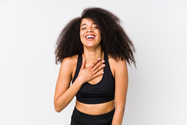 Joven mujer deportiva afroamericana se ríe a carcajadas manteniendo la mano en el pecho.