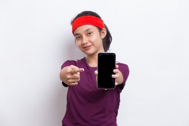 Joven mujer deportiva asiática demostrando teléfono móvil sobre fondo blanco.