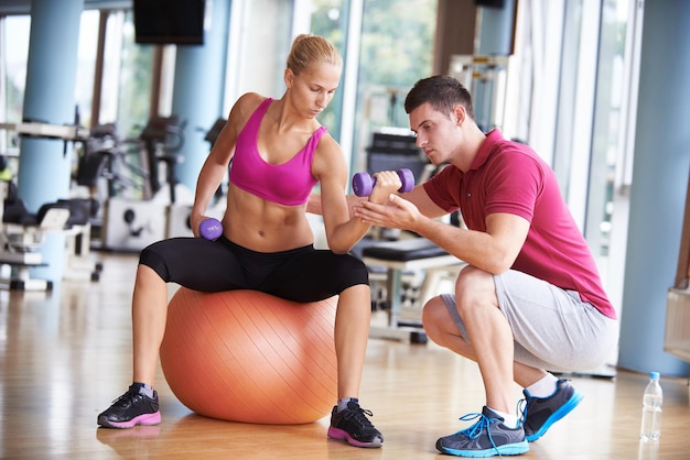 joven mujer deportiva con entrenador ejercicio levantamiento de pesas en el gimnasio