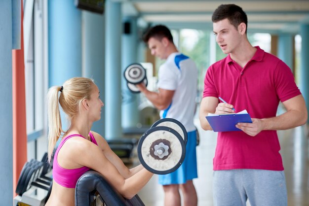 Foto joven mujer deportiva con entrenador ejercicio levantamiento de pesas en el gimnasio