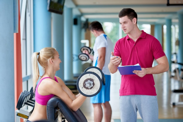 Foto joven mujer deportiva con entrenador ejercicio levantamiento de pesas en el gimnasio