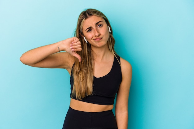 Joven mujer deportiva escuchando música con auriculares aislados mostrando un gesto de aversión, pulgares hacia abajo