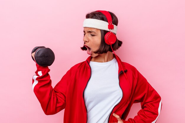 Joven mujer deportiva de raza mixta escuchando música aislada sobre fondo rosa