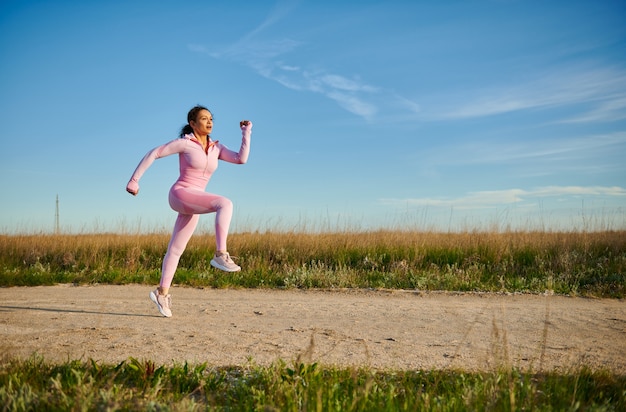 Joven mujer deportiva en ropa deportiva rosa trotar al aire libre en un hermoso día soleado de principios de verano. Deporte. concepto de entrenamiento de salud, resistencia y cardio con espacio de copia