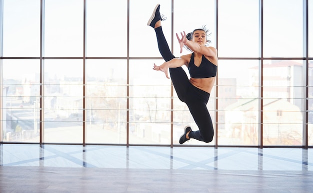 Foto joven mujer deportiva en ropa deportiva saltando y haciendo trucos atléticos contra la ventana en el aire.