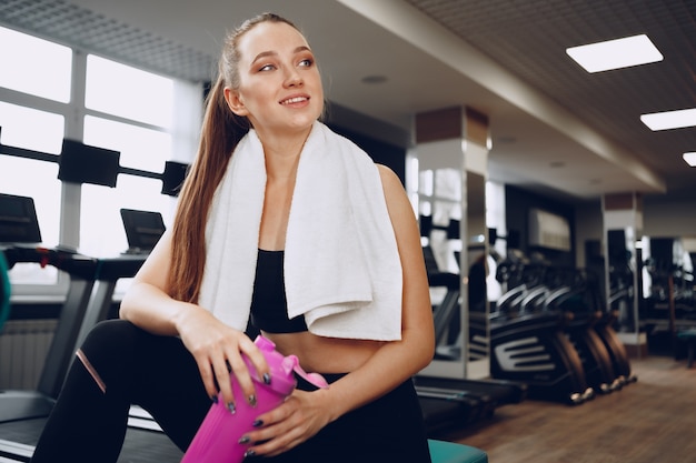 Joven mujer deportiva tomando una copa en un gimnasio después del entrenamiento