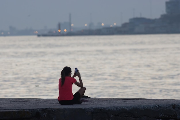 Joven mujer deportiva tomando fotos en el móvil en el río al amanecer.