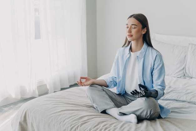 Joven mujer discapacitada está practicando yoga en posición de loto en la cama en su dormitorio Alivio del estrés en casa