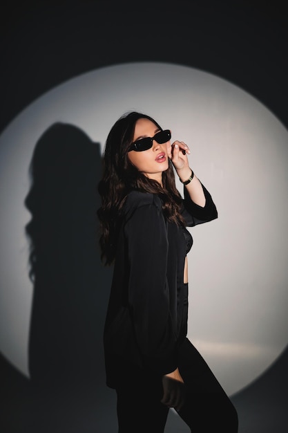 Joven mujer elegante con estilo en un traje negro Disparo de estudio Una mujer en un traje negro y gafas negras sobre un fondo blanco