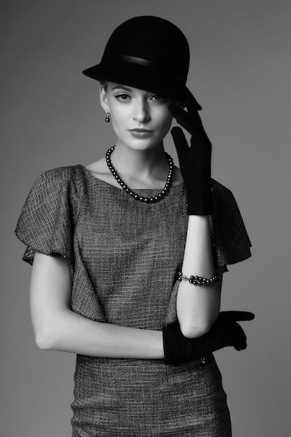 Joven mujer elegante, moda retro, sombrero, guantes, vestido. Imagen en blanco y negro.