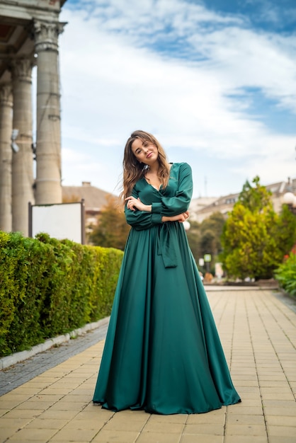 Joven mujer elegante relajante y posando para la cámara cerca de columnas en vestido verde en un día de verano perfecto, estilo de vida