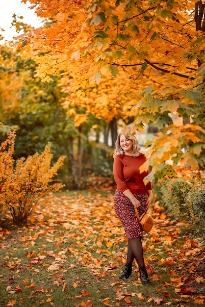 Joven mujer elegante de talla grande camina en un parque de otoño Tira hojas Una hermosa niña sonriente con un traje marrón sobre un fondo de hojas doradas