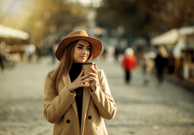 mujer elegante vestida con un abrigo y un sombrero de fieltro camina por la ciudad y café mientras viaja. otoño | Foto Premium