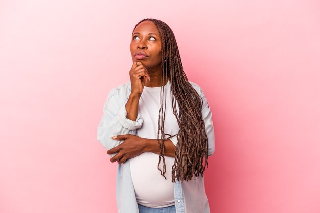 Joven mujer embarazada afroamericana aislada sobre fondo rosa mirando hacia los lados con expresión dudosa y escéptica.