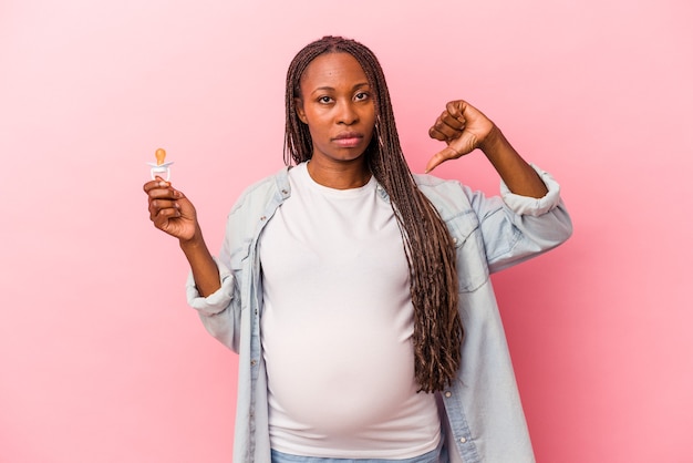 Joven mujer embarazada afroamericana sosteniendo chupete aislado sobre fondo rosa mostrando un gesto de aversión, pulgares hacia abajo. Concepto de desacuerdo.