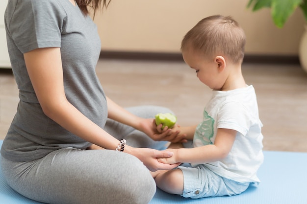 Joven mujer embarazada asiática meditando en casa con su hijo niño. Concepto de maternidad saludable