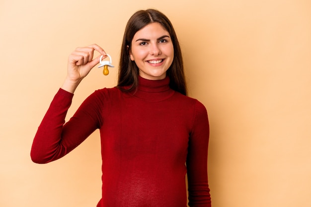 Joven mujer embarazada caucásica aislada en la pared beige feliz, sonriente y alegre