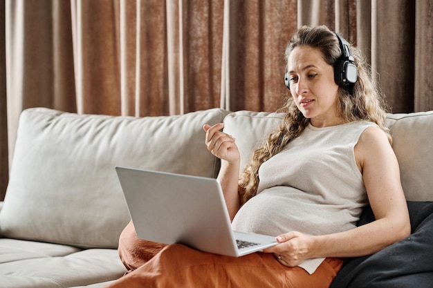 Joven mujer embarazada confiada en auriculares comunicándose con alguien