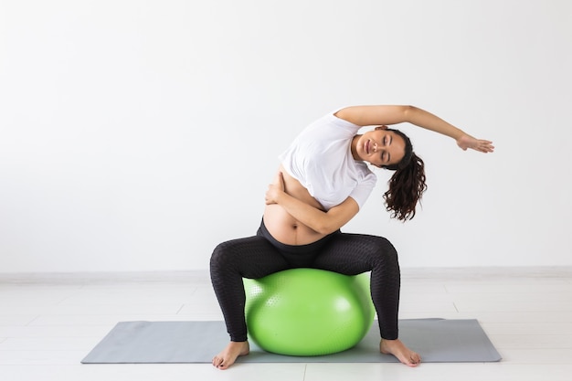 Joven mujer embarazada flexible haciendo gimnasia sobre una alfombra en el suelo sobre fondo blanco el concepto