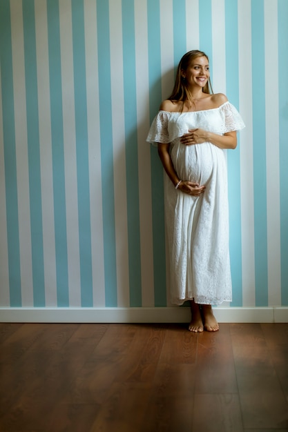 Joven mujer embarazada de pie junto a la pared