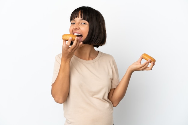 Joven mujer embarazada de raza mixta aislada sobre fondo blanco comiendo una rosquilla