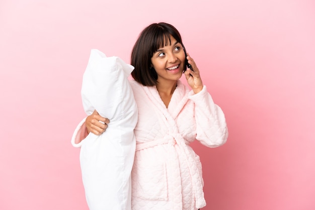 Foto joven mujer embarazada de raza mixta aislada sobre fondo rosa en pijama y sosteniendo una almohada mientras habla con el móvil