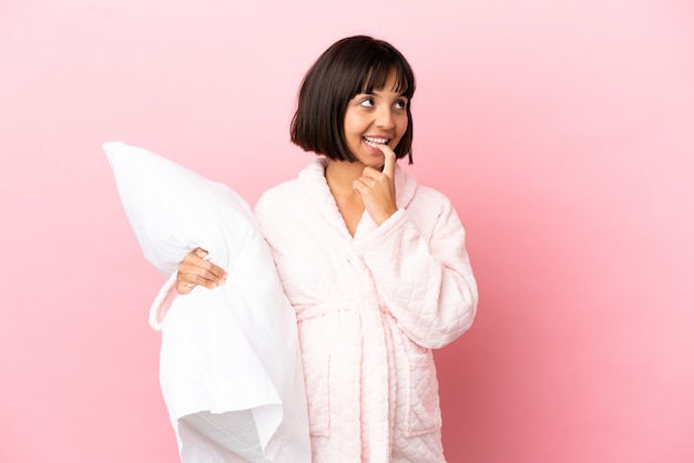 Foto joven mujer embarazada de raza mixta aislada sobre fondo rosa en pijama y sosteniendo una almohada mientras piensa